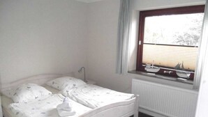 Un dormitorio con una cama individual, una ventana con persianas, un radiador y una mesita de noche con una lámpara.