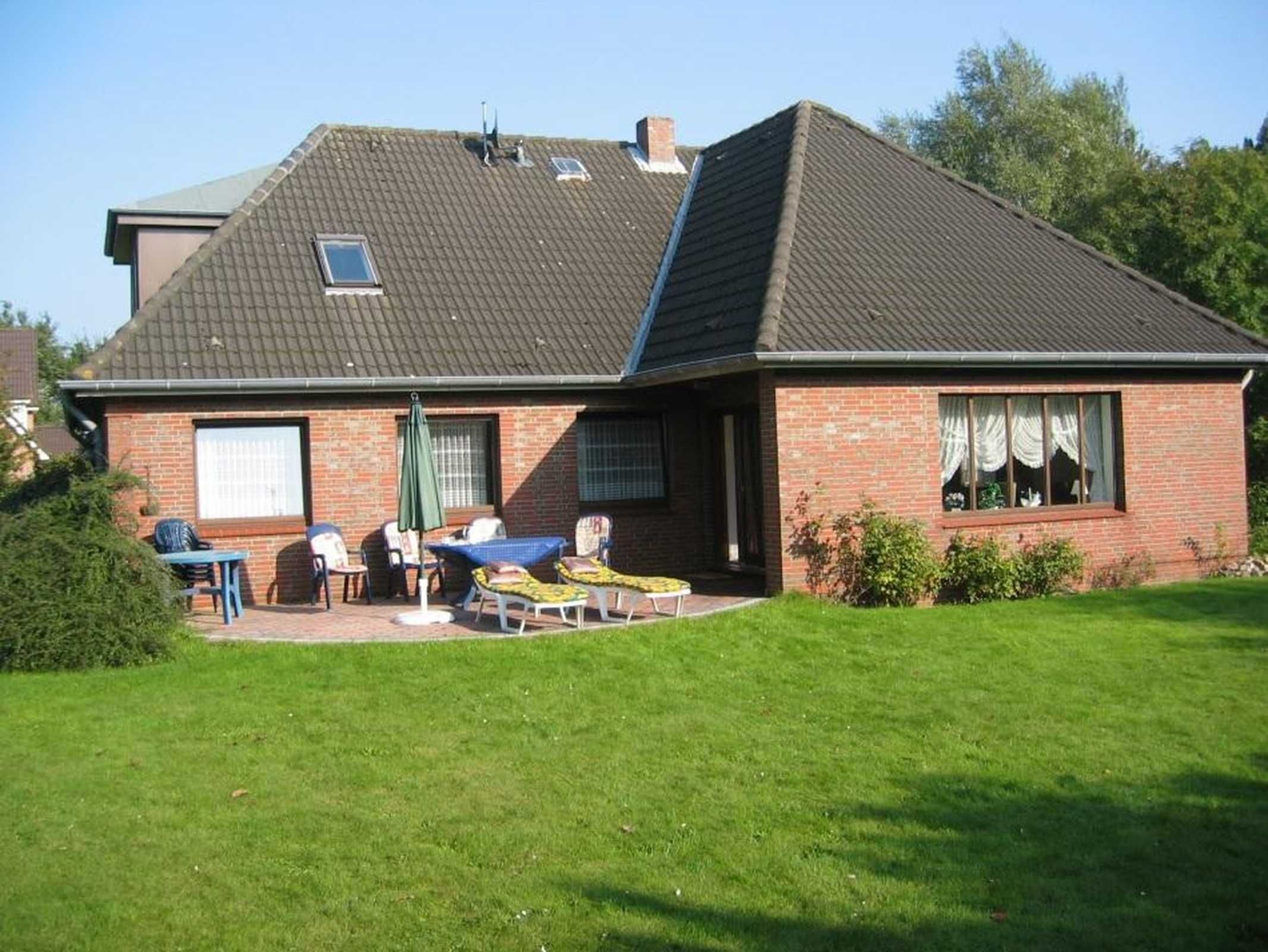 Une maison avec un toit en pente, une façade en briques et un petit patio aménagé avec du mobilier d’extérieur.