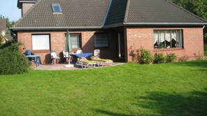 Una casa con techo inclinado, fachada de ladrillo y un pequeño patio con mobiliario exterior.