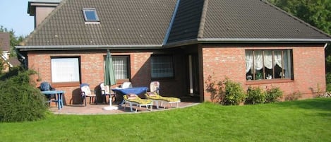Une maison avec un toit en pente, une façade en briques et un petit patio aménagé avec du mobilier d’extérieur.