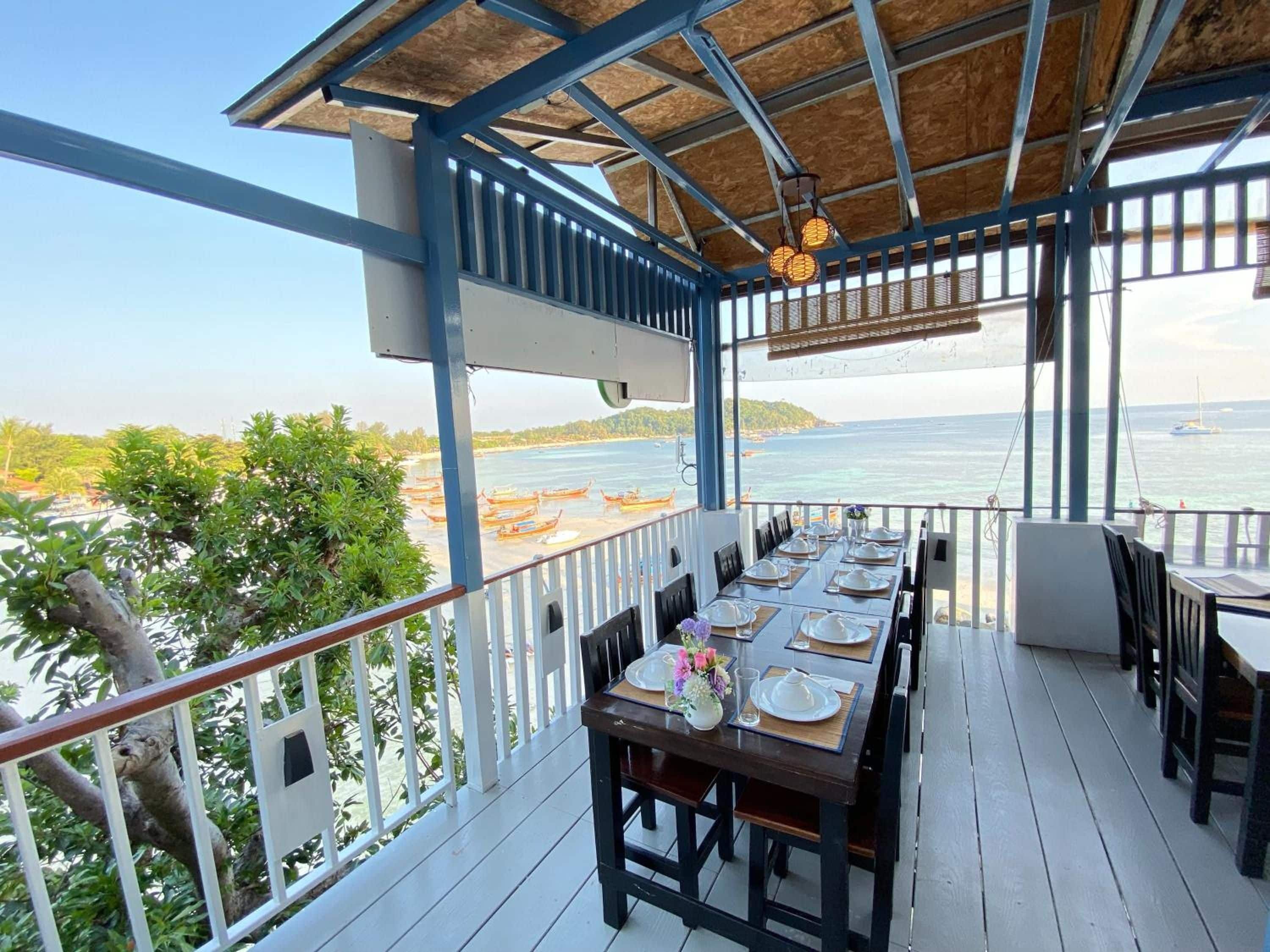 Un espacio exterior techado para comer con mesas dispuestas para dos, con vista a una playa y al mar.