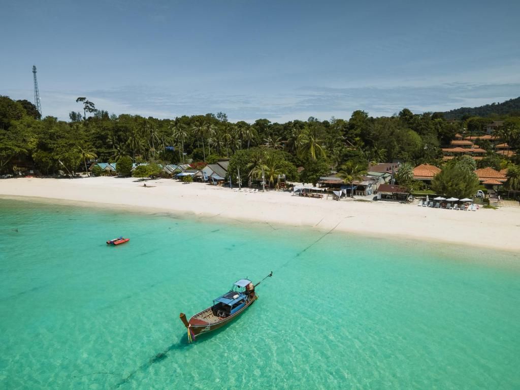 Et kystområde med en båd for anker nær stranden, omgivet af en sandstrand og en række huse.