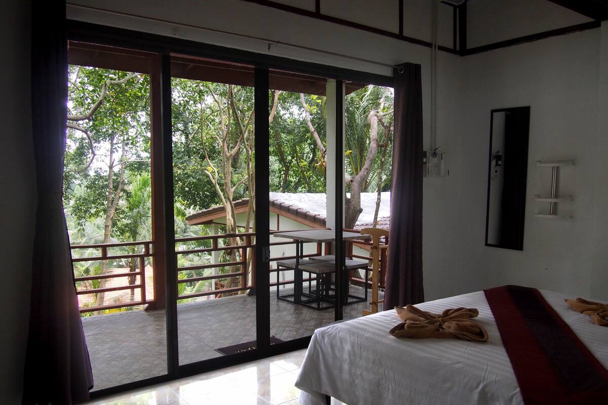 A hotel room with a bed, a table, chairs, and a view of the outdoors through a sliding door.