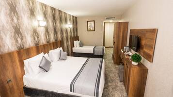 Quarto de hotel com uma cama grande, cabeceira de madeira, mesa de cabeceira com espelho e uma pequena planta.