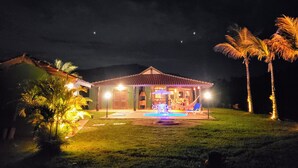 A house with a swimming pool, surrounded by palm trees and a mountain in the background.