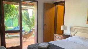 A hotel room with a bed, a nightstand, a lamp, and a view of the garden through a glass door.