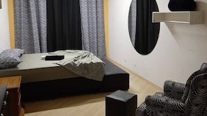 Un dormitorio con cama, ventilador de techo, mesita de noche, silla y estante en la pared.