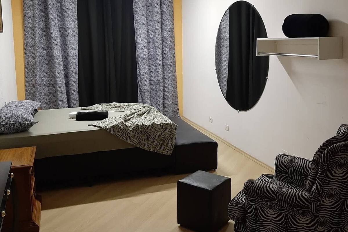 A bedroom with a bed, a ceiling fan, a bedside table, a chair, and a wall-mounted shelf.