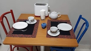Una mesa de comedor con cuatro sillas, un tostador, una tetera y un juego de tazas.