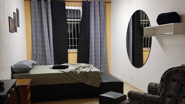 Una habitación con cama, escritorio, silla, espejo y ventana con cortinas.