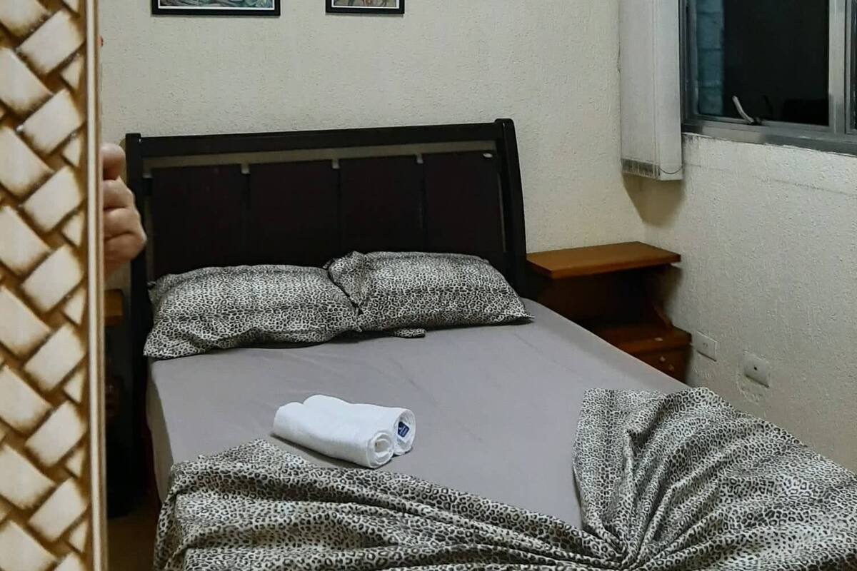 A bedroom with a bed, a window, and three framed artworks on the wall.