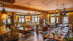 Un restaurant avec des tables en bois, des lampes suspendues et de grandes fenêtres.