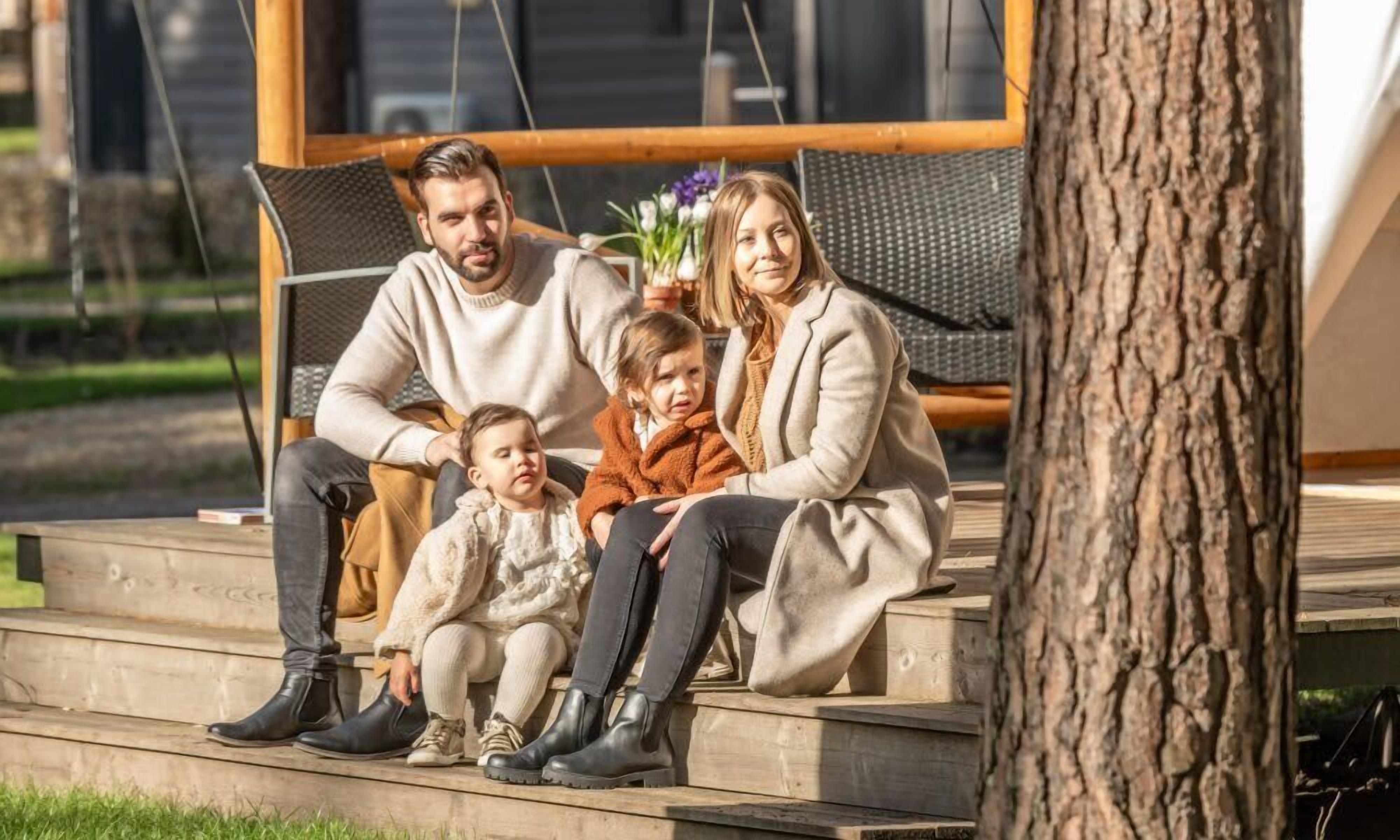 A family of four seated on outdoor wooden steps with a tree to the right.
