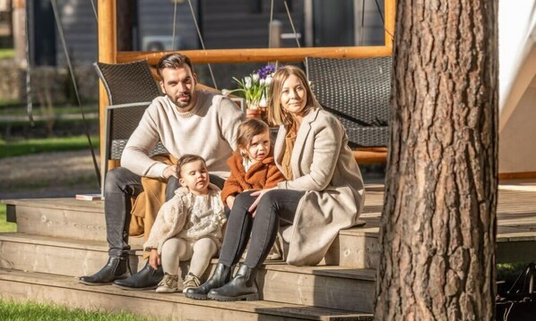 A family of four seated on outdoor wooden steps with a tree to the right.