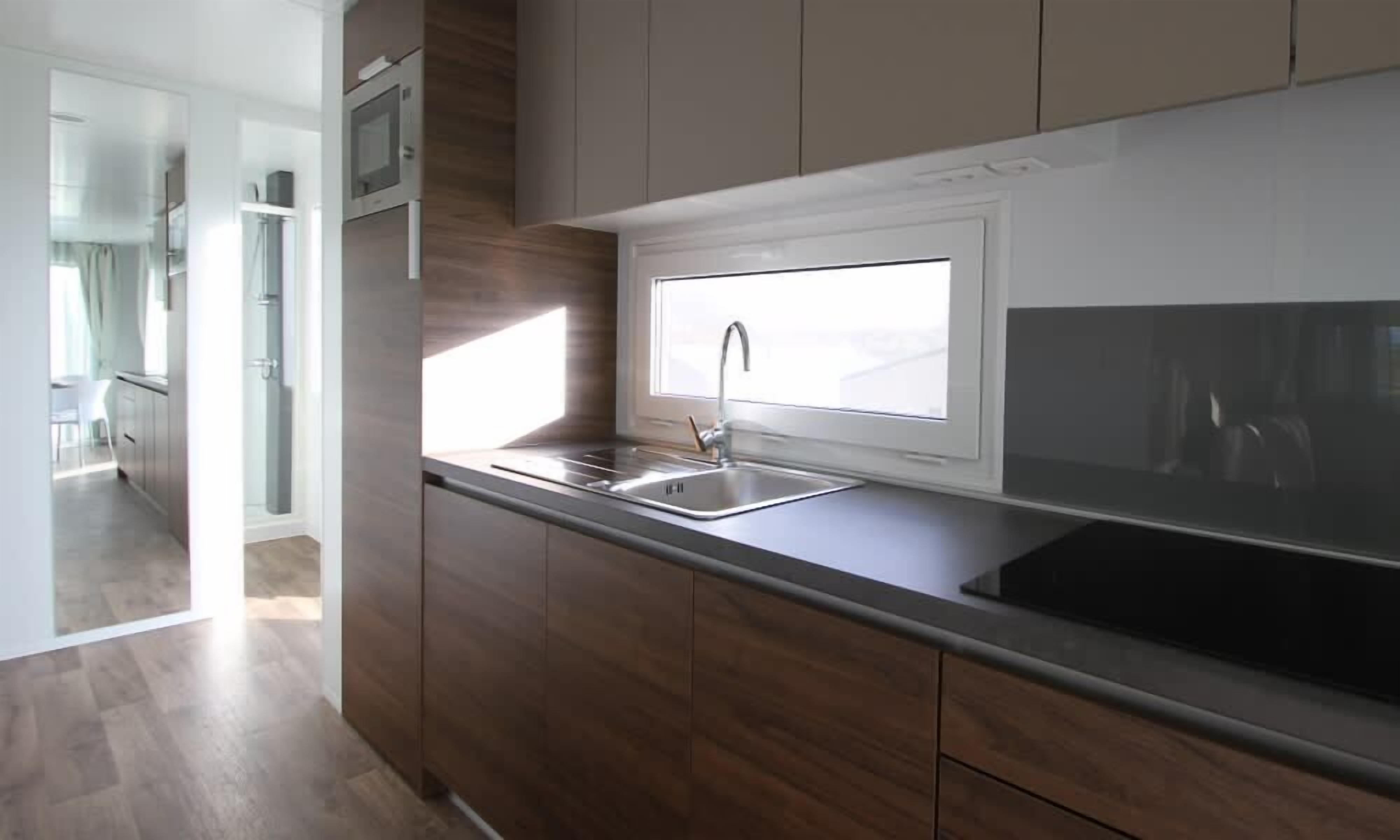 Een moderne keuken met houten kastjes, een roestvrijstalen spoelbak en een raam boven de spoelbak.