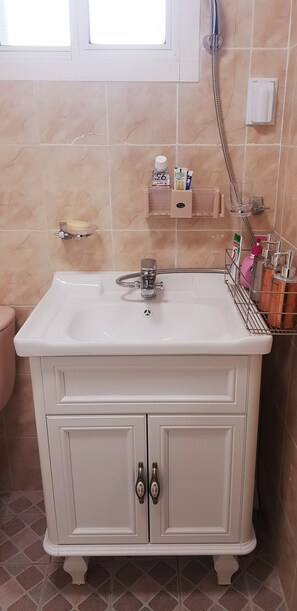 A bathroom with a white sink, two cabinets, a toilet, a shower, and a window.
