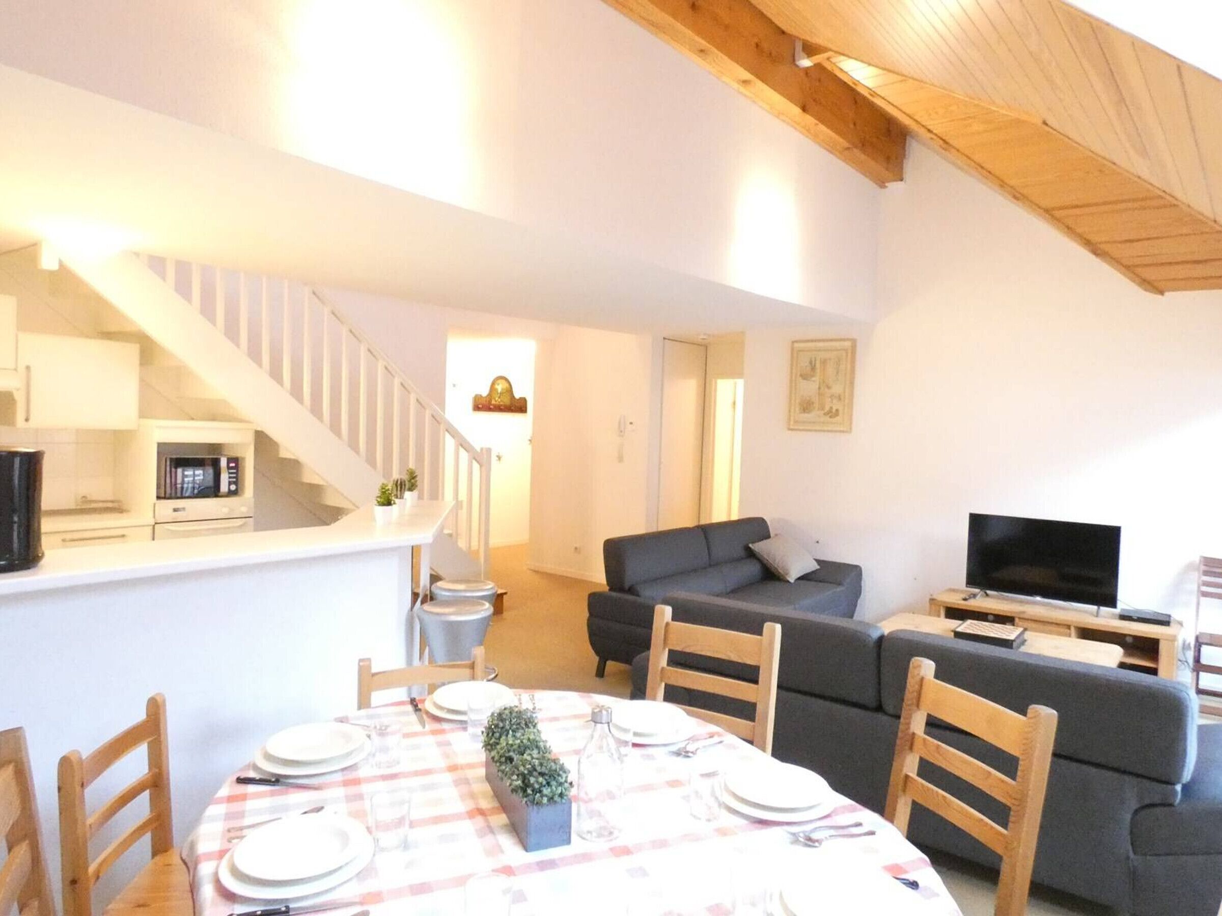 A living room with a sofa, a TV, and a dining area with a table set for four.