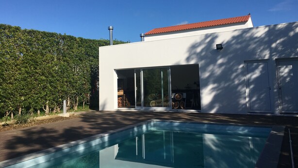 Et moderne hus med swimmingpool, en overdækket terrasse og udsigt til en skovklædt bakke.