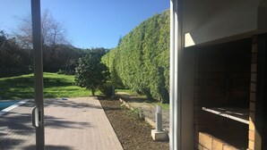 En terrasse med en murstenspejs, en pool og udsigt over et grønt landskab med træer.