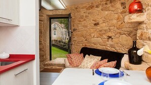 Un comedor con pared de piedra, una mesa lista para dos personas y vista a un edificio de piedra en el exterior.