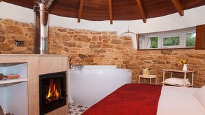 Un dormitorio con pared de piedra, chimenea, una bañera grande y ventana con cortinas.