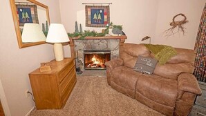 A living room with a fireplace, a sofa, a wooden cabinet, and a lamp. - 3407 Pine Hill 2 Bedroom Home by RedAwning (South Lake Tahoe)