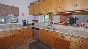 A kitchen with wooden cabinets, a granite countertop, a dishwasher, and a window with a curtain. - 3407 Pine Hill 2 Bedroom Home by RedAwning (South Lake Tahoe)