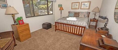 Une chambre à coucher comprenant un lit, un bureau, une chaise, une commode, une lampe et une fenêtre donnant sur l’extérieur.