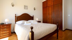 A neatly made bed with a wooden headboard, a dresser with drawers, and a large wooden wardrobe. - Apartamento Mar Azul (Figueira da Foz)
