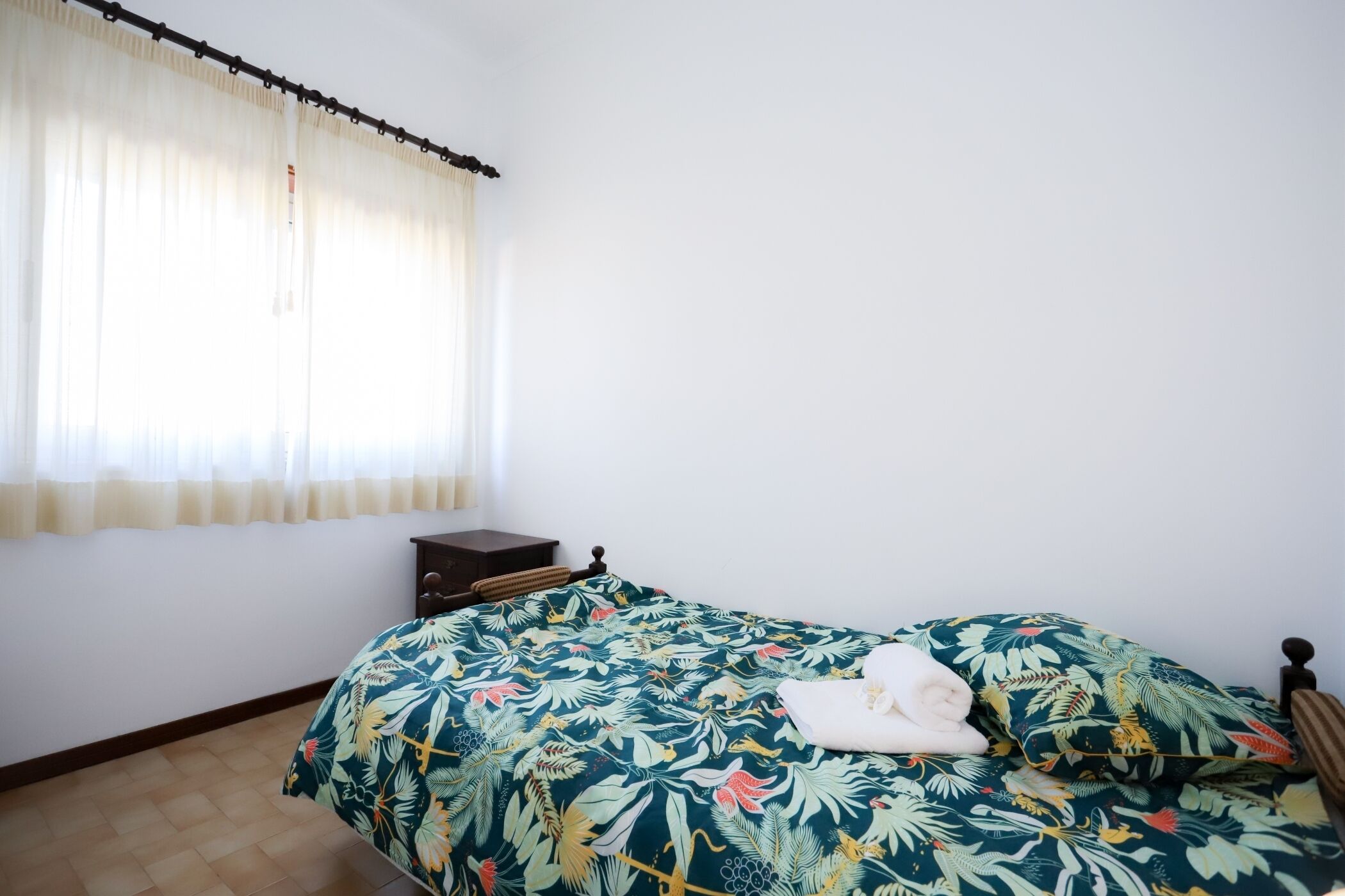 A bedroom with a bed, a nightstand, and a window with curtains.