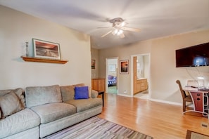 A living room with a sofa, a ceiling fan, a flat-screen TV, and a dining area with a table and chairs.