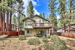 A two-story house with a balcony, surrounded by tall pine trees.