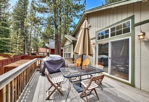 Une terrasse avec une table et des chaises, un barbecue couvert et une porte-fenêtre coulissante donnant sur un patio abrité.