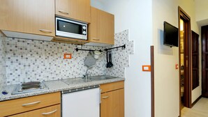 A kitchen with wooden cabinets, a microwave, a sink, and a tiled backsplash. - Cavour Square Apartment (Rome)