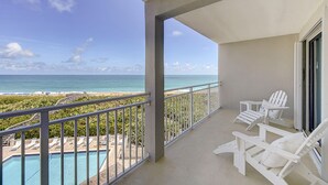 Un balcón con vista al océano y la playa, sillones blancos para tomar el sol y una piscina.