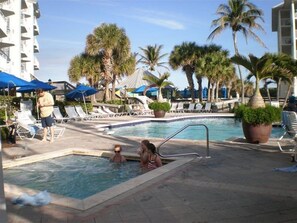 Relax by the pool surrounded by palm trees and umbrellas, with lounge chairs and a pool ladder for easy access.