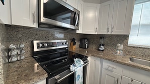 A kitchen with white cabinets, a stainless steel microwave, a stove, and a coffee maker. - R & K’s Marathon Paradise 2/2 Duplex w/35` Dock & Cabana Club Included (Marathon)