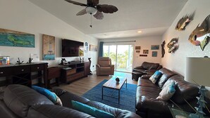 A living room with a sofa, armchairs, a coffee table, a TV, a ceiling fan, and artwork on the walls. - R & K’s Marathon Paradise 2/2 Duplex w/35` Dock & Cabana Club Included (Marathon)