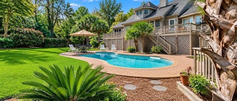 A residential property with a swimming pool, a covered patio, and a well-maintained lawn.