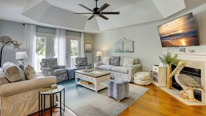 Ein modernes Wohnzimmer mit Deckenventilator, Kamin und großem Fernseher an der Wand.