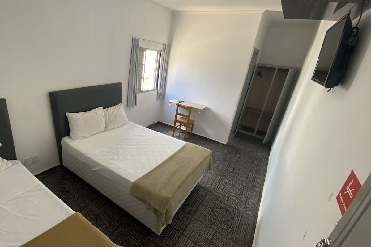 Ett hotellrum med två separata sängar, ett skrivbord, en stol, en tv som är monterad på väggen och ett fönster med gardiner.