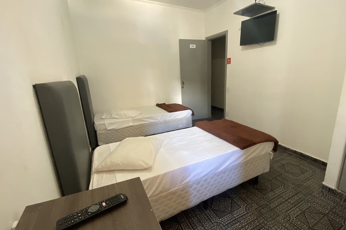 Ett hotellrum med två sängar, en tv som är monterad på väggen och en fjärrkontroll på ett litet bord.