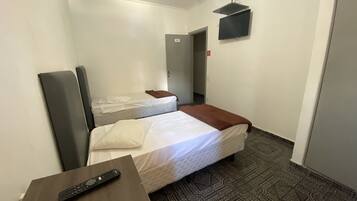 Habitación de hotel con dos camas, un televisor fijado a la pared y un control remoto sobre una mesita.