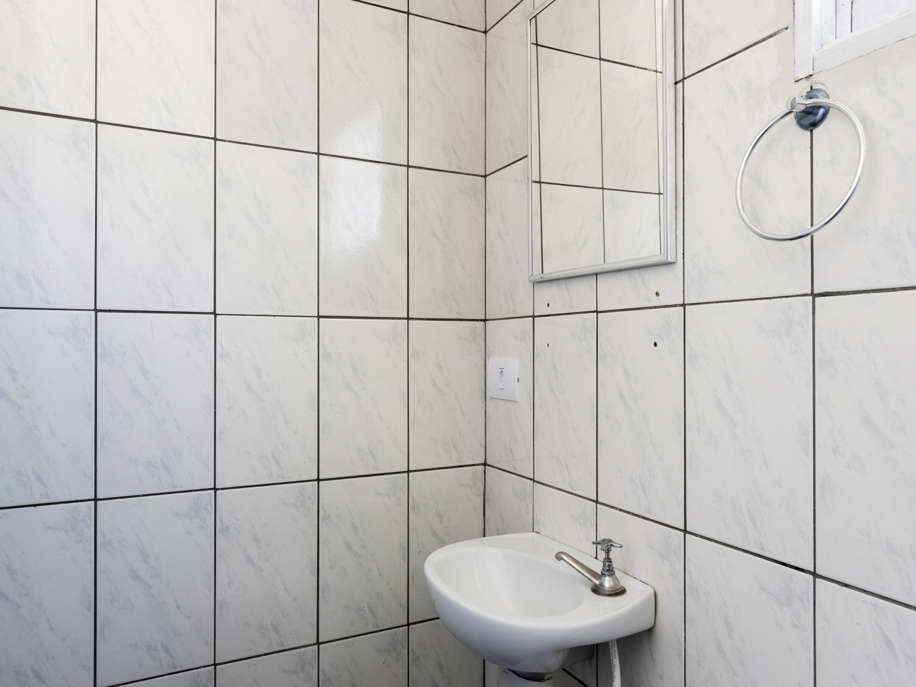 A bathroom with white marble tiles, a white sink, and a mirror.