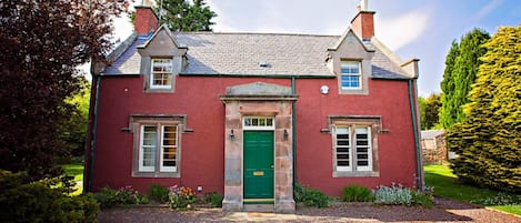 A two-story house with a red exterior, a green door, and a gravel driveway.