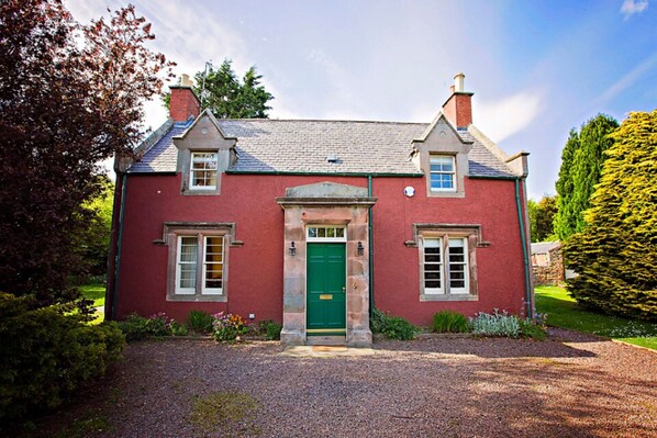 A two-story house with a red exterior, a green door, and a gravel driveway.