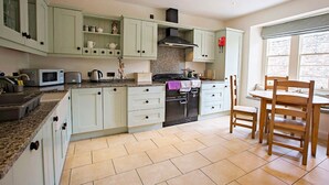Une cuisine avec des meubles de couleur vert clair, un plan de travail en granit, une cuisinière et un coin repas avec des chaises en bois.