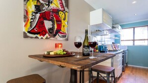 Une cuisine avec une table en bois, deux tabourets, une bouteille de vin et des verres.