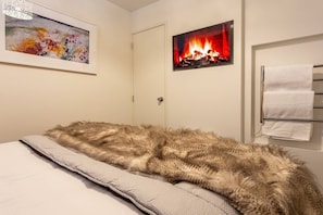 A bedroom with a bed, a painting, a fireplace image, and a towel rack. - Central City Apartment with Parking & Great Views (Queenstown)