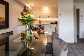 A modern kitchen with white cabinets, a built-in oven, and a dining area with a glass table and chairs. - Central City Apartment with Parking & Great Views (Queenstown)